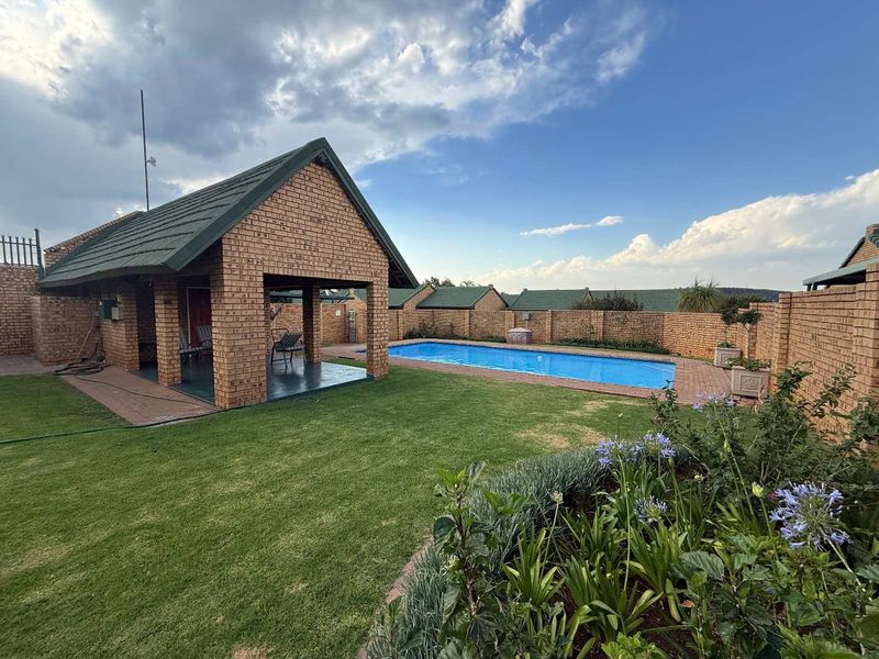 A well-maintained outdoor area featuring a swimming pool, a covered brick patio, and a landscaped garden enclosed by a secure brick boundary wall.