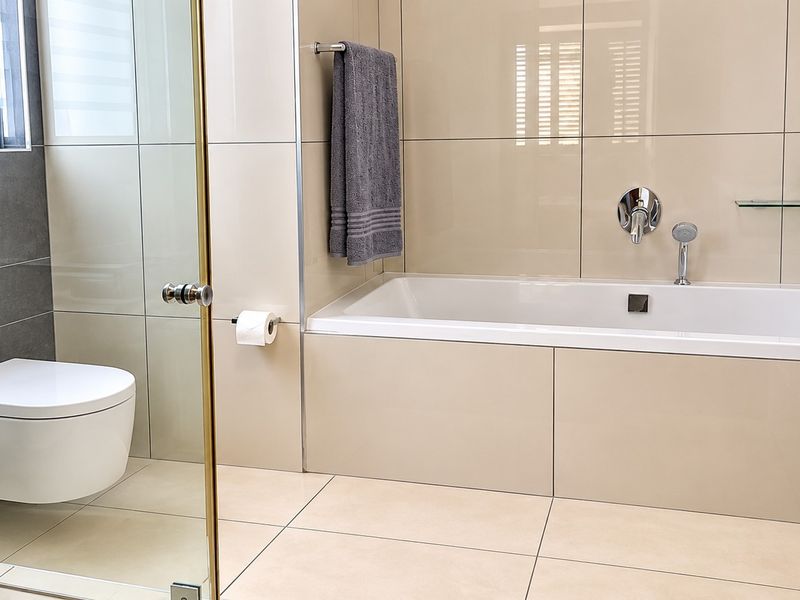 Modern bathroom featuring a wall-mounted toilet with concealed cistern, a built-in bathtub with chrome fixtures, and neutral large-format wall and floor tiles.