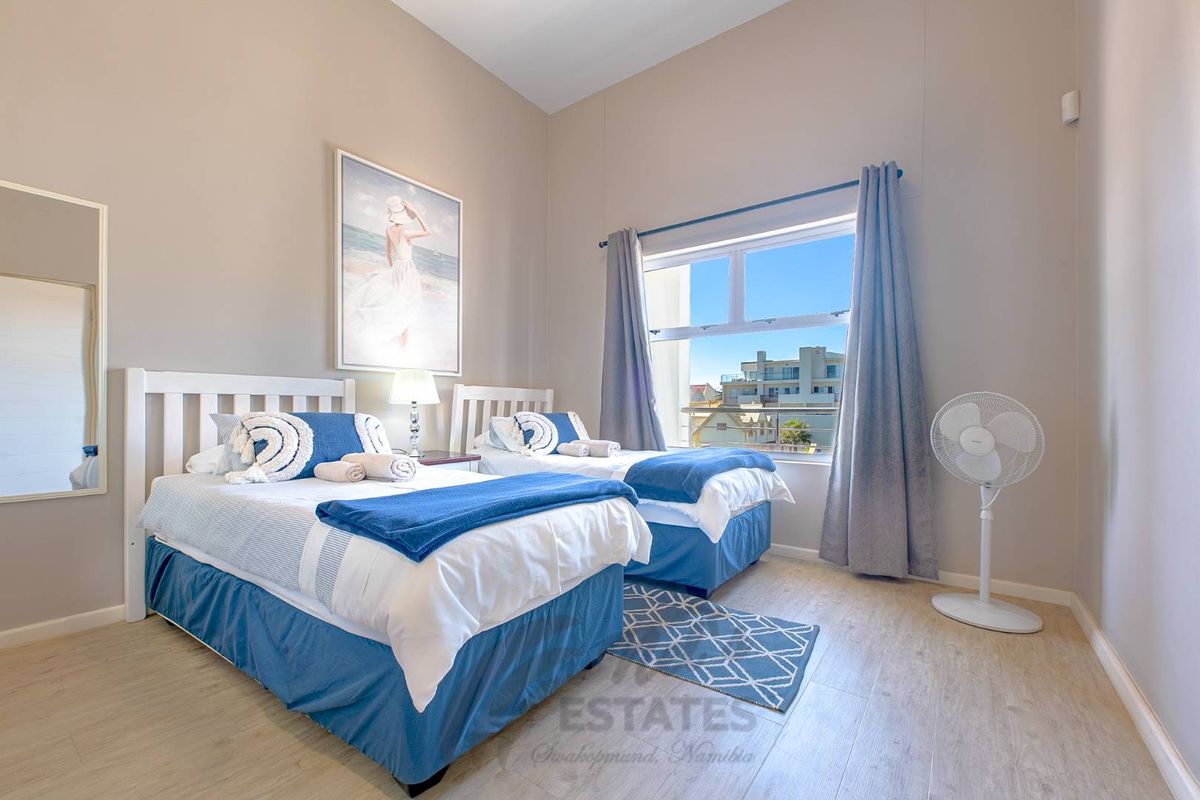 A bright bedroom featuring light wood-look flooring, high ceilings, and a large window offering an urban view.