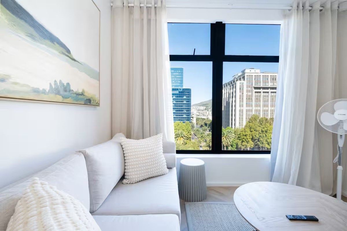 A bright living room featuring large floor-to-ceiling windows with city views and elegant herringbone flooring.