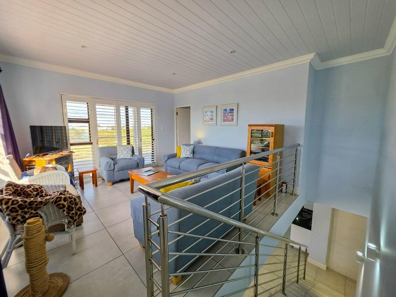 Spacious living area featuring tiled flooring, a tongue and groove ceiling, and a modern stainless steel balustrade overlooking the staircase.
