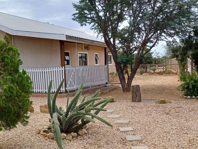 A rear exterior view of the property featuring a landscaped garden with stone pathways, mature trees, and a secure perimeter fence.