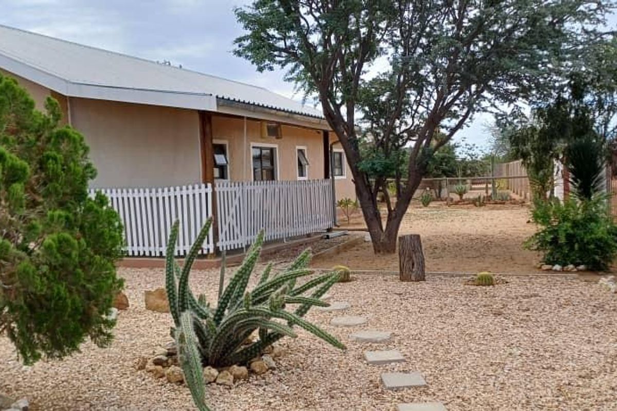 A rear exterior view of the property featuring a landscaped garden with stone pathways, mature trees, and a secure perimeter fence.