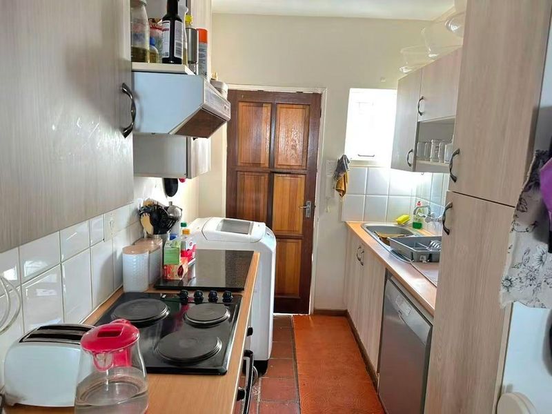 A functional galley-style kitchen featuring built-in cabinetry, an electric hob with extractor fan, and a double sink with tiled backsplash.