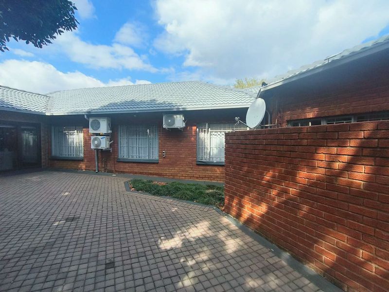 A view of the rear exterior featuring a brick facade, paved courtyard area, and mounted air conditioning units.