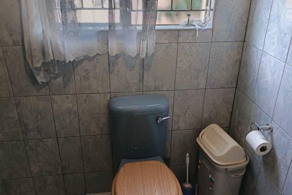 A compact bathroom featuring floor-to-ceiling wall tiles, tiled flooring, and a window with security bars.