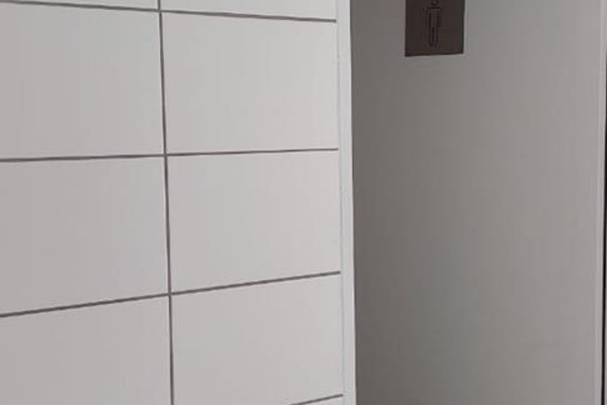 A clean, functional office restroom featuring white wall tiling, a pedestal basin, and a door leading to the toilet area.