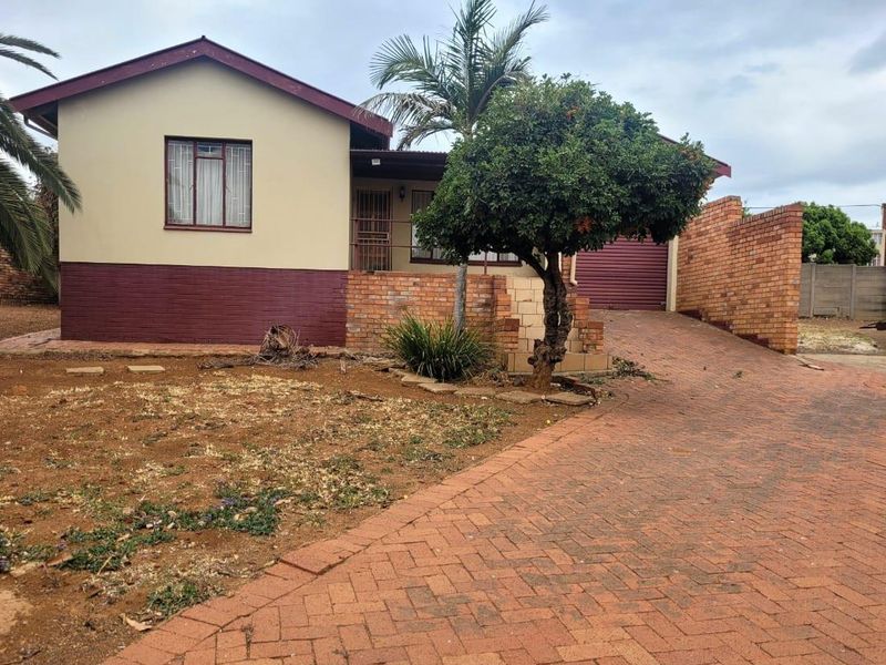 Front view of a single-story house featuring a brick driveway, garage, and established garden area with boundary walling.