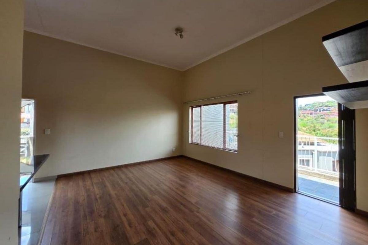 Spacious living area featuring warm-toned laminate flooring, high ceilings, and direct access to an outdoor balcony with scenic views.