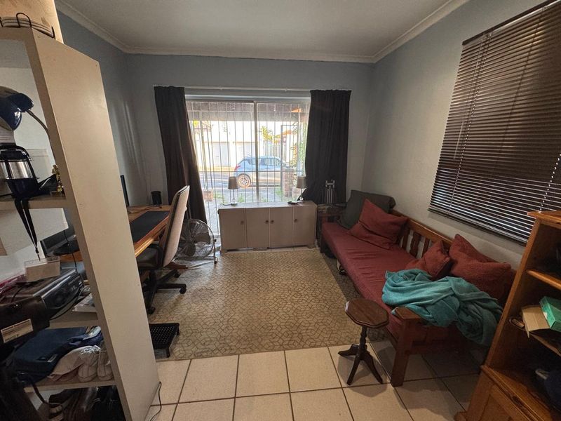 A functional living room featuring tiled flooring, coving, and a sliding glass door with integrated security gate, providing access to the exterior.