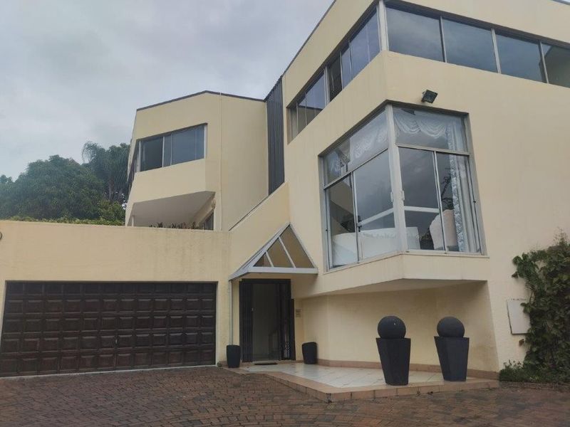 Front elevation of a multi-level modern house featuring a paved driveway, double garage, and large glass windows.