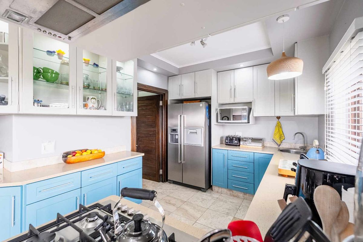 A well-maintained kitchen featuring blue and white cabinetry, stone countertops, a gas hob, and integrated stainless steel appliances.