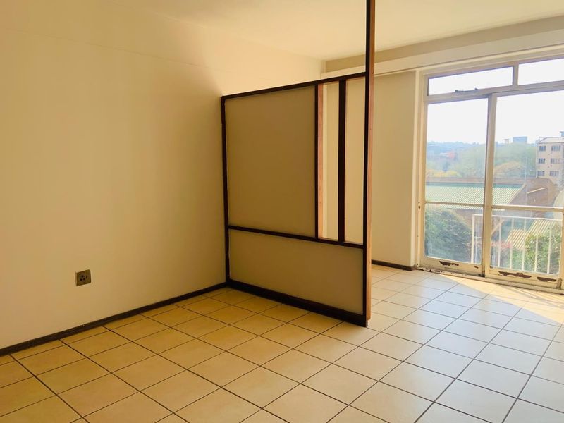 An empty living area featuring tiled flooring, a built-in room divider, and a sliding glass door leading to a balcony.