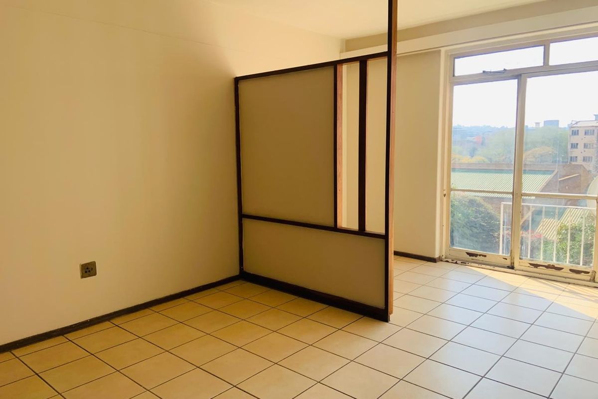 An empty living area featuring tiled flooring, a built-in room divider, and a sliding glass door leading to a balcony.