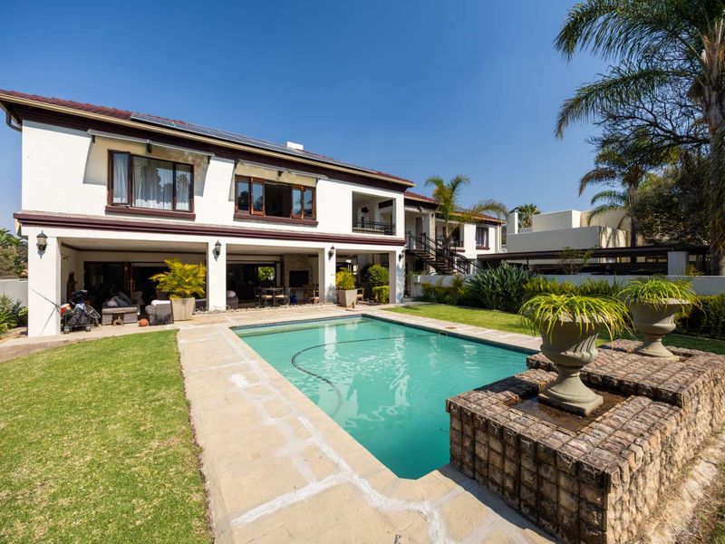 Rear view of a two-story house featuring a swimming pool, covered patio area, brick water feature, and well-maintained garden.