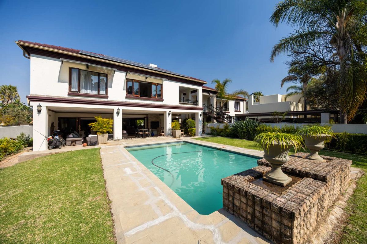 Rear view of a two-story house featuring a swimming pool, covered patio area, brick water feature, and well-maintained garden.