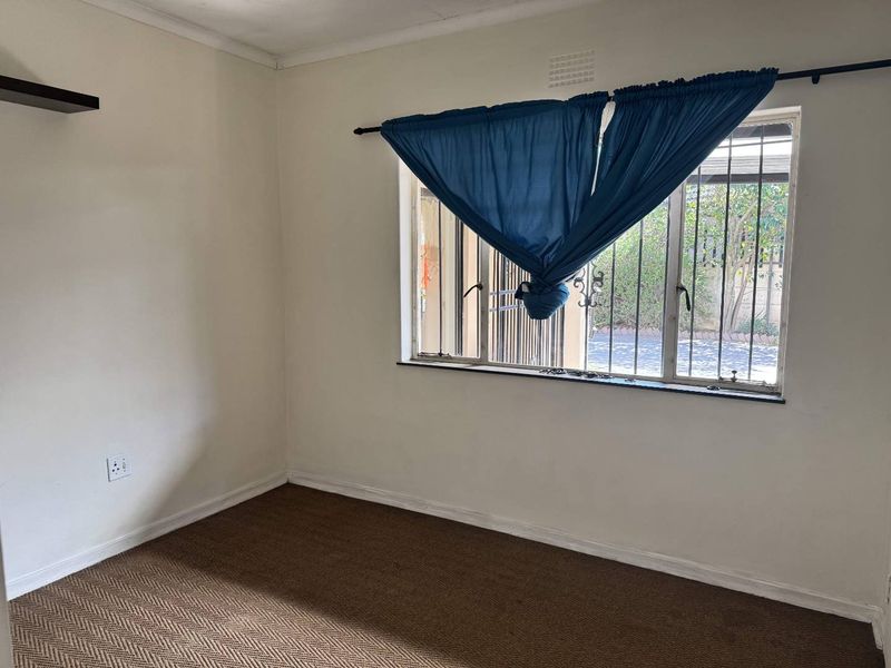 An empty bedroom featuring carpet flooring, a wall-mounted shelf, and a window fitted with metal security bars.