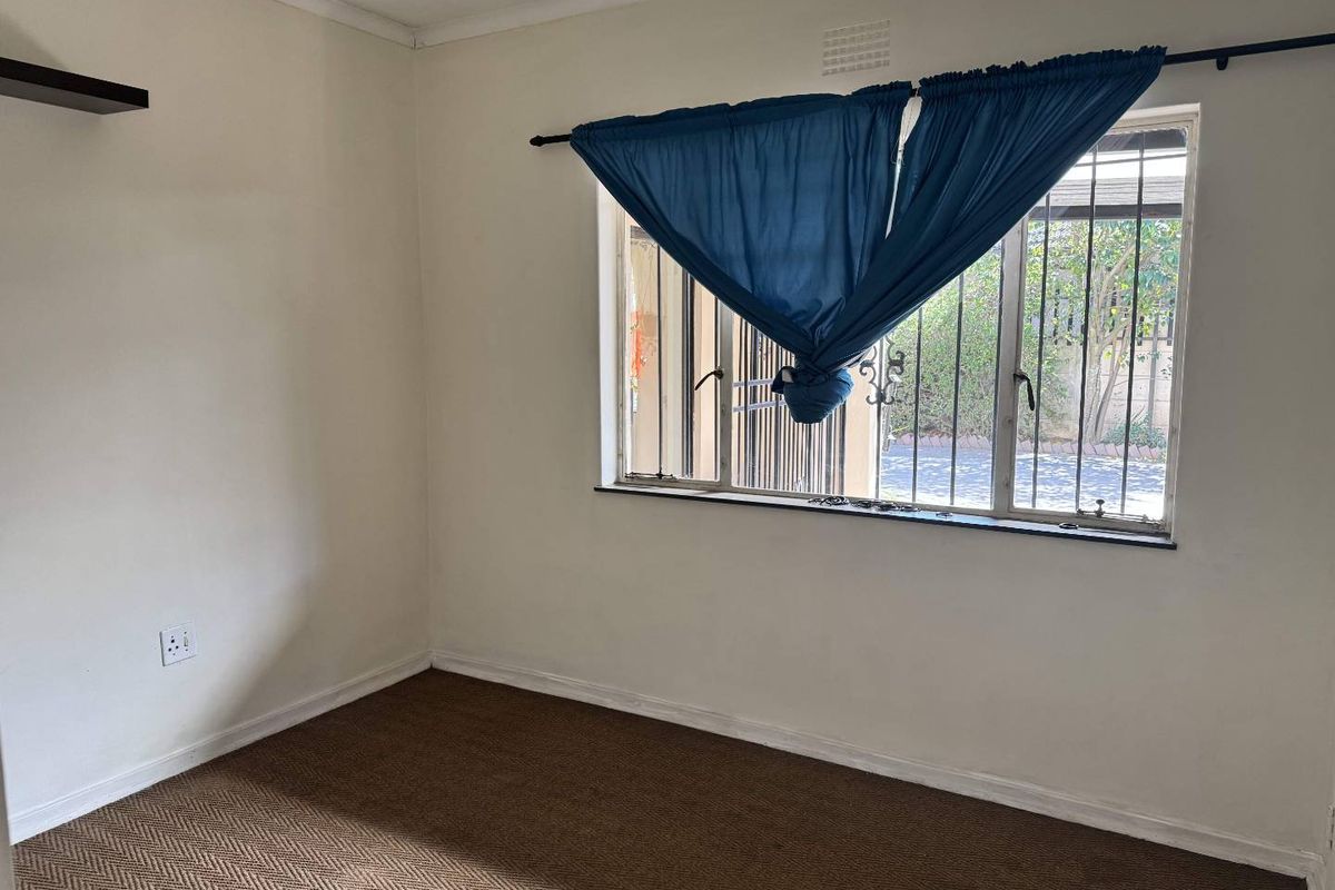 An empty bedroom featuring carpet flooring, a wall-mounted shelf, and a window fitted with metal security bars.