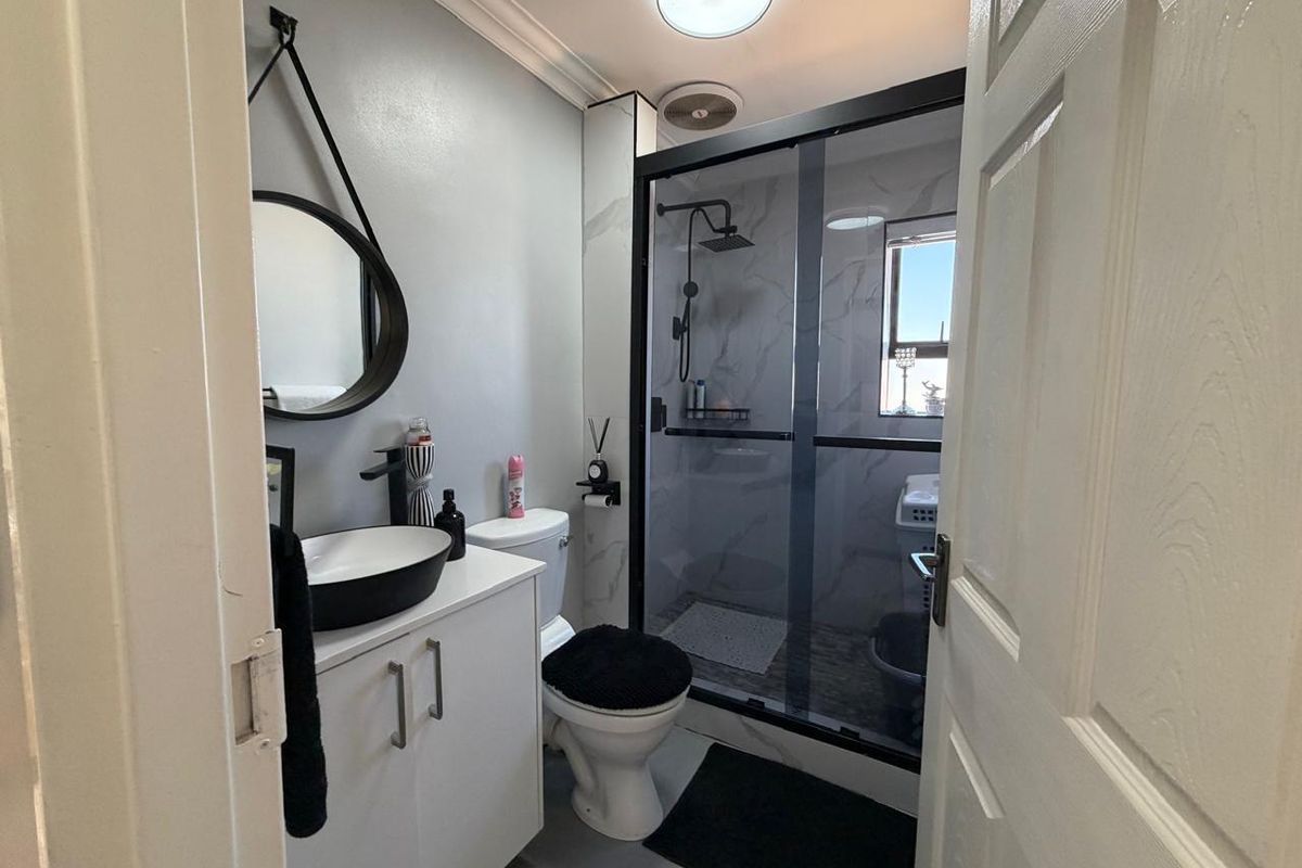 Modern bathroom featuring a vanity with vessel sink, toilet, and a glass-enclosed shower with contemporary black fixtures.