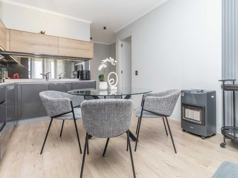 Modern open-plan kitchen and dining area featuring sleek cabinetry, integrated appliances, mirror splashback, and light wood-look laminate flooring.
