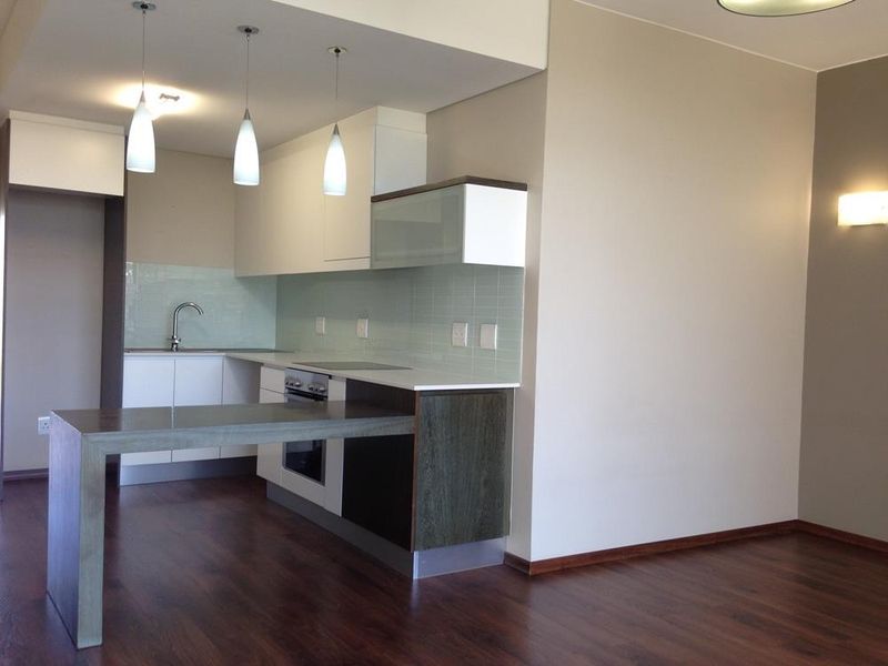 Modern open-plan kitchen featuring sleek cabinetry, integrated appliances, glass splashback, and a breakfast bar, seamlessly flowing into the adjacent living area.