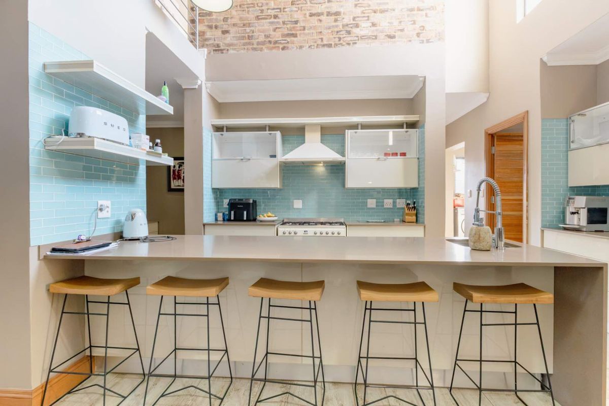 Modern kitchen featuring a large island with breakfast bar seating, light blue subway tile backsplash, gas stove, and a striking exposed brick feature wall.