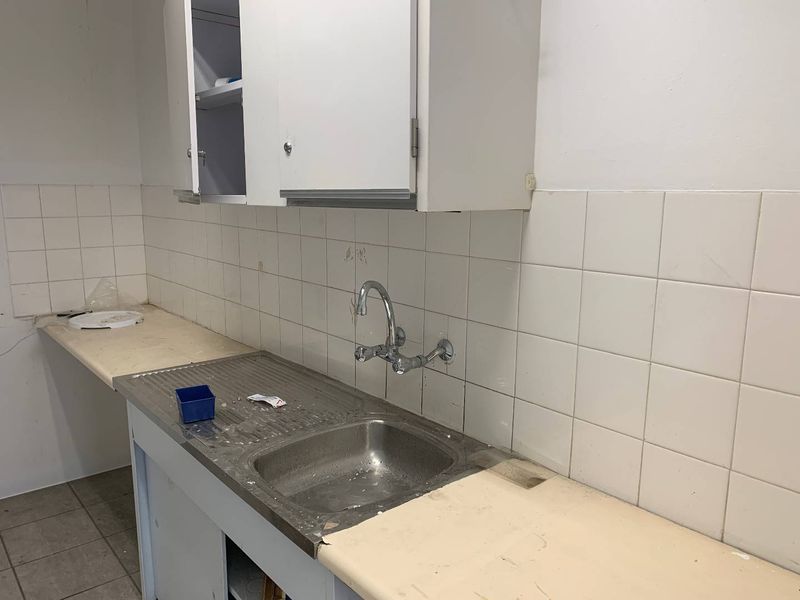 A functional scullery or utility area featuring a stainless steel sink, tiled backsplash, and basic cabinetry, requiring cosmetic updates to improve its condition.