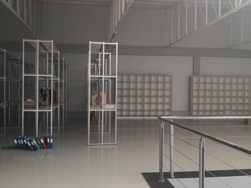 Spacious industrial utility area featuring high ceilings with exposed steel trusses, polished epoxy flooring, and extensive built-in metal shelving units.