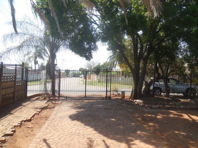 View of the property entrance featuring a metal security gate, brick paved driveway, and mature trees bordering the street.
