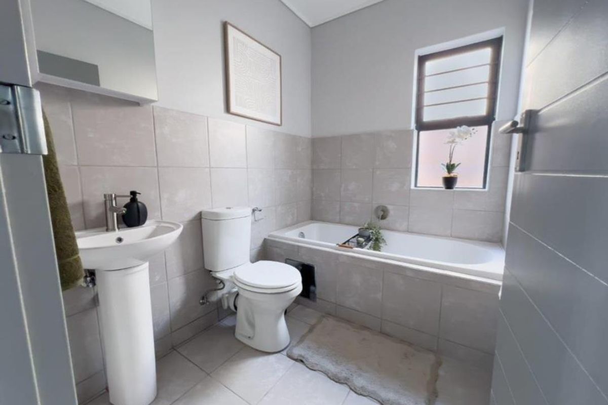 A clean and modern bathroom featuring a pedestal basin, toilet, and a tiled built-in bathtub with neutral finishes.