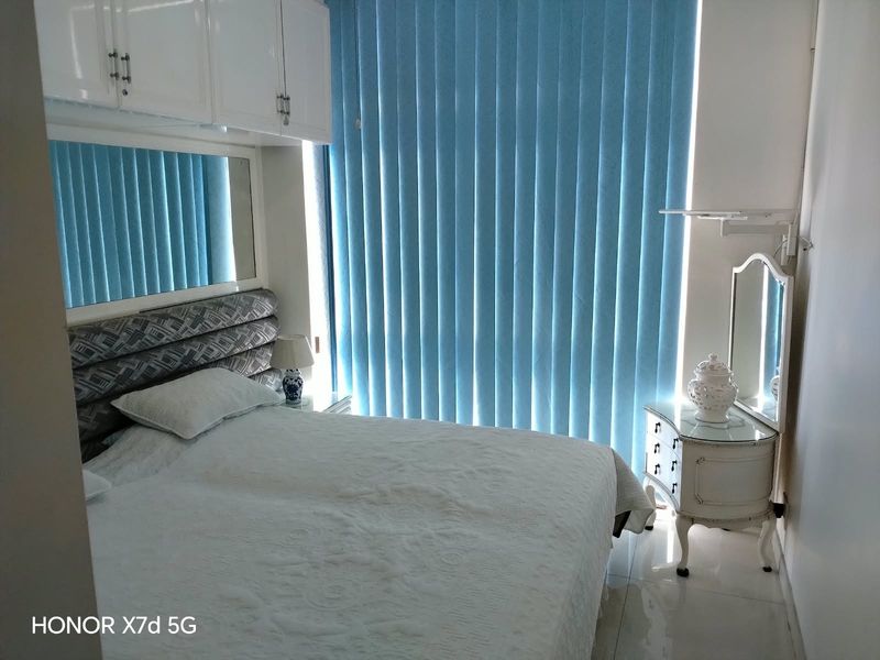 A bedroom featuring built-in overhead cabinetry, a mirrored wall panel, and vertical blinds, finished with tiled flooring.