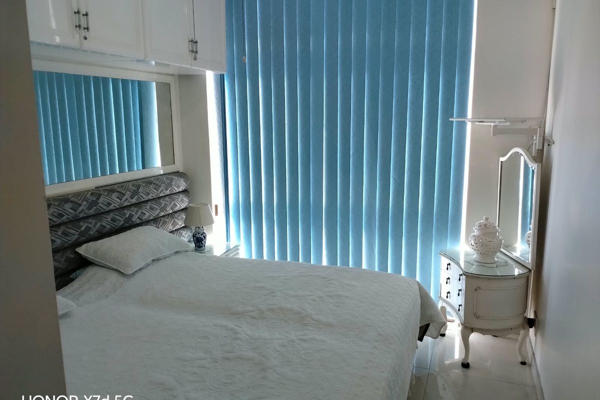 A bedroom featuring built-in overhead cabinetry, a mirrored wall panel, and vertical blinds, finished with tiled flooring.