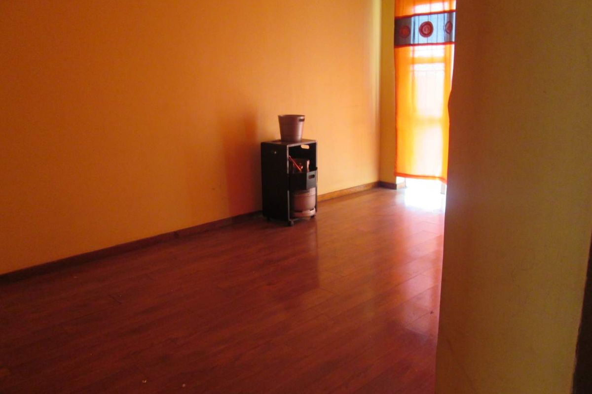 An empty living room featuring warm-toned walls and laminate wood flooring, illuminated by natural light from a window with orange curtains.