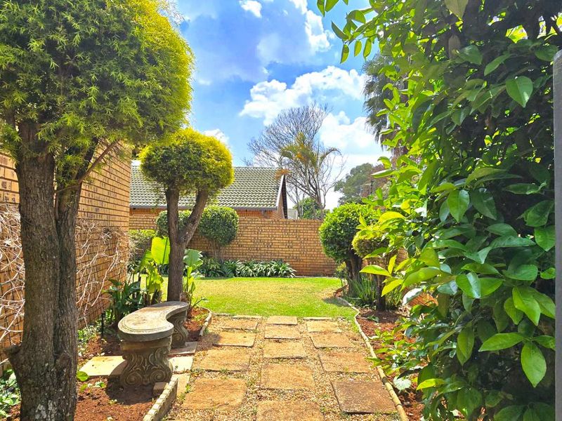 A well-maintained private garden featuring a paved walkway, established trees, and brick boundary walls, providing a peaceful outdoor space.