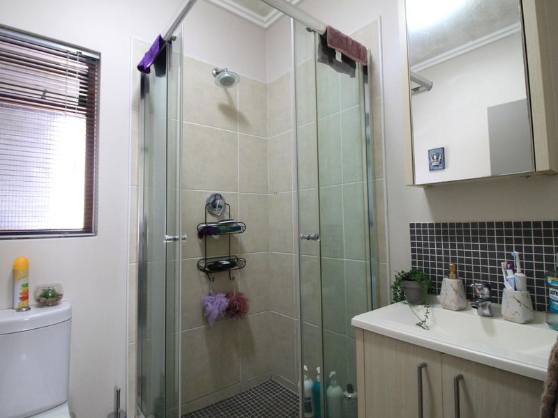 A functional bathroom featuring a glass-enclosed shower, a vanity cabinet with basin, a medicine cabinet, and a toilet with neutral wall tiling.