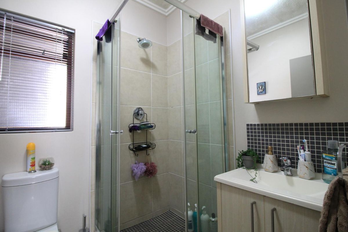 A functional bathroom featuring a glass-enclosed shower, a vanity cabinet with basin, a medicine cabinet, and a toilet with neutral wall tiling.