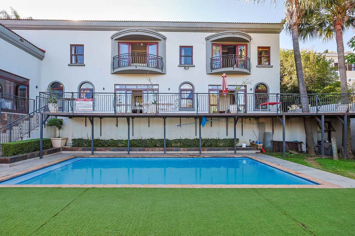 Rear view of a multi-story house featuring a raised deck, balconies, and a swimming pool set within a landscaped garden area.