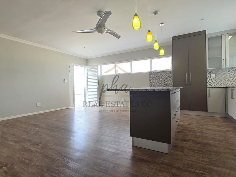 Spacious open-plan living area featuring a modern kitchen with a central island, built-in cabinetry, and durable laminate flooring throughout.