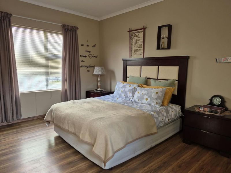 A well-maintained bedroom featuring durable laminate flooring and large windows with venetian blinds, offering a comfortable and neutral living space.