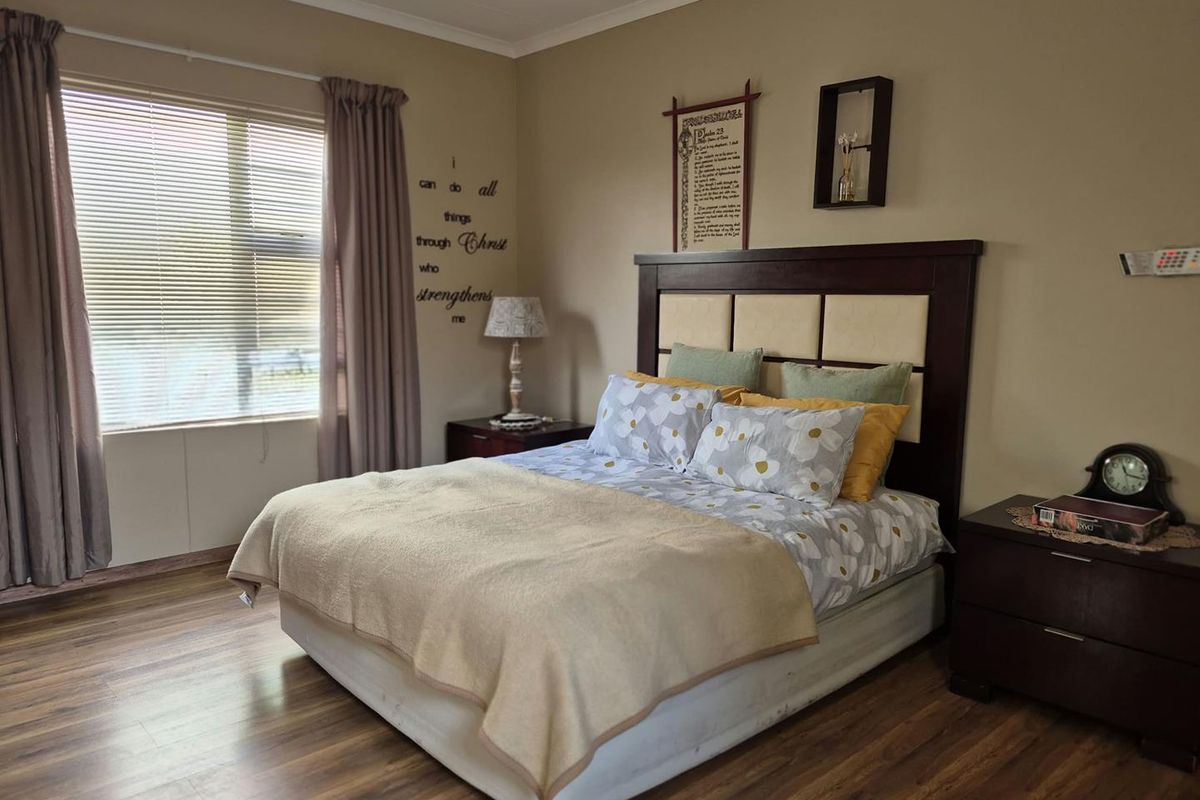 A well-maintained bedroom featuring durable laminate flooring and large windows with venetian blinds, offering a comfortable and neutral living space.