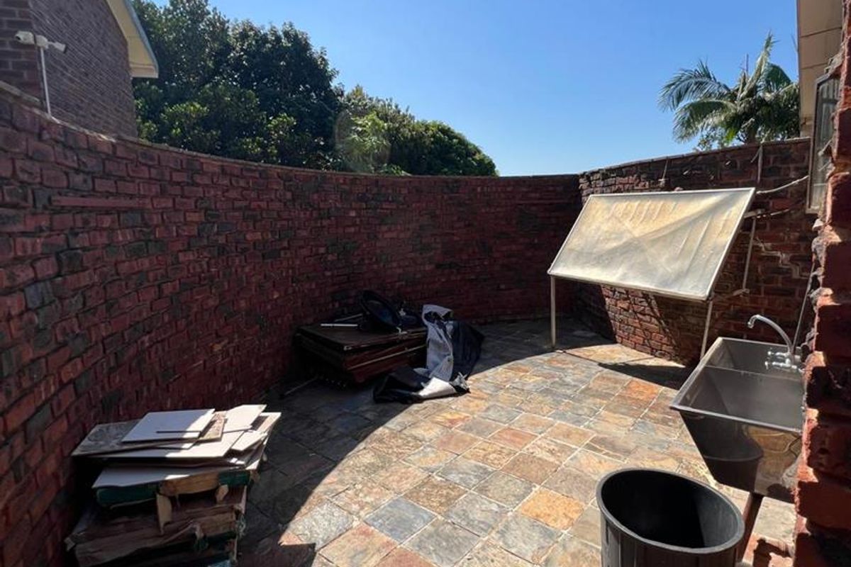 A rear courtyard area featuring stone tile flooring, a brick boundary wall, and a built-in stainless steel utility sink.