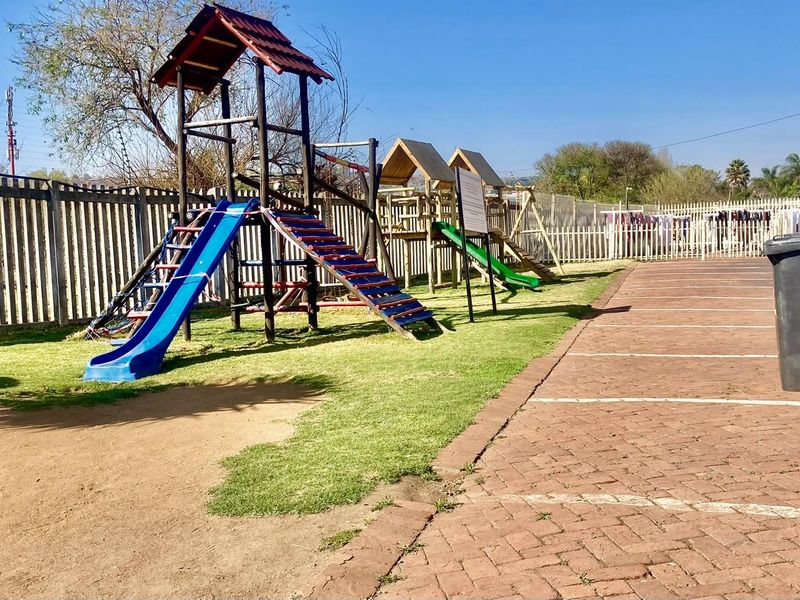 Communal outdoor area featuring a children's playground, paved parking bays, and perimeter fencing.