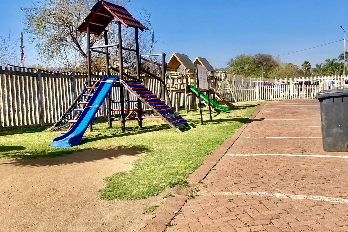 Communal outdoor area featuring a children's playground, paved parking bays, and perimeter fencing.