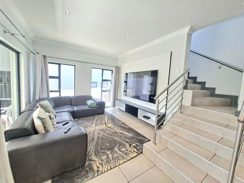 Modern living room featuring tiled floors, a built-in media wall, and an adjacent staircase with a contemporary stainless steel balustrade.