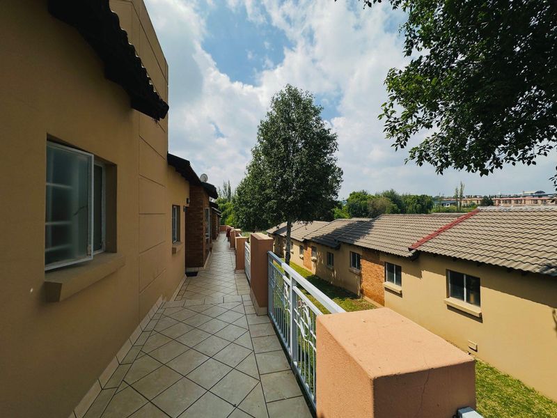 A spacious outdoor balcony featuring tiled flooring and a secure metal balustrade, overlooking the surrounding apartment complex grounds.