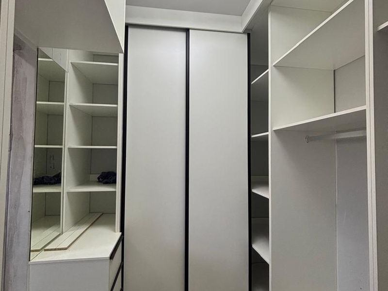 A modern walk-in closet or dressing area featuring extensive built-in cabinetry, shelving, and a contemporary geometric ceiling light fixture.