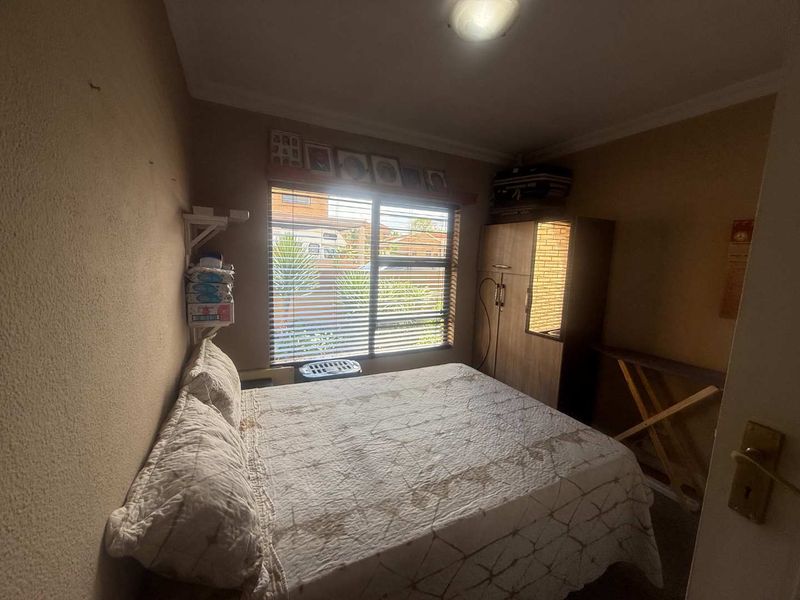 A compact bedroom featuring a window with venetian blinds and standard ceiling lighting, requiring cosmetic updates to improve the overall finish and appeal.