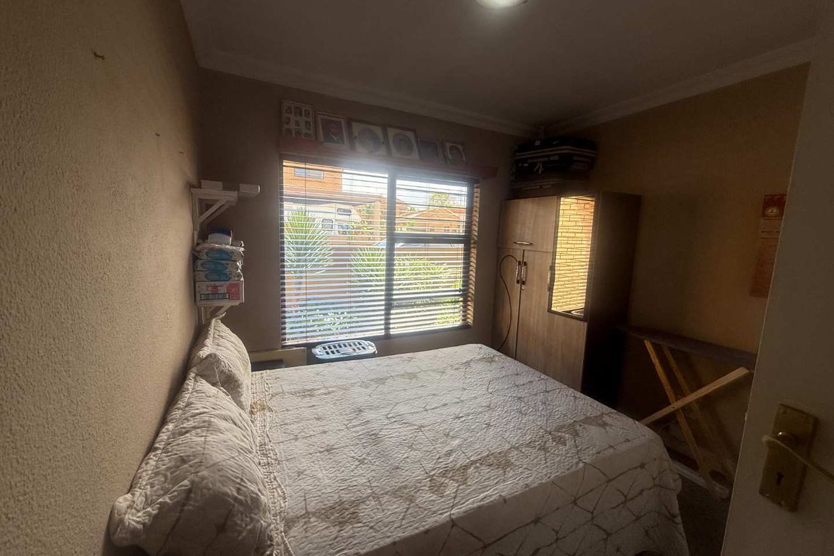 A compact bedroom featuring a window with venetian blinds and standard ceiling lighting, requiring cosmetic updates to improve the overall finish and appeal.
