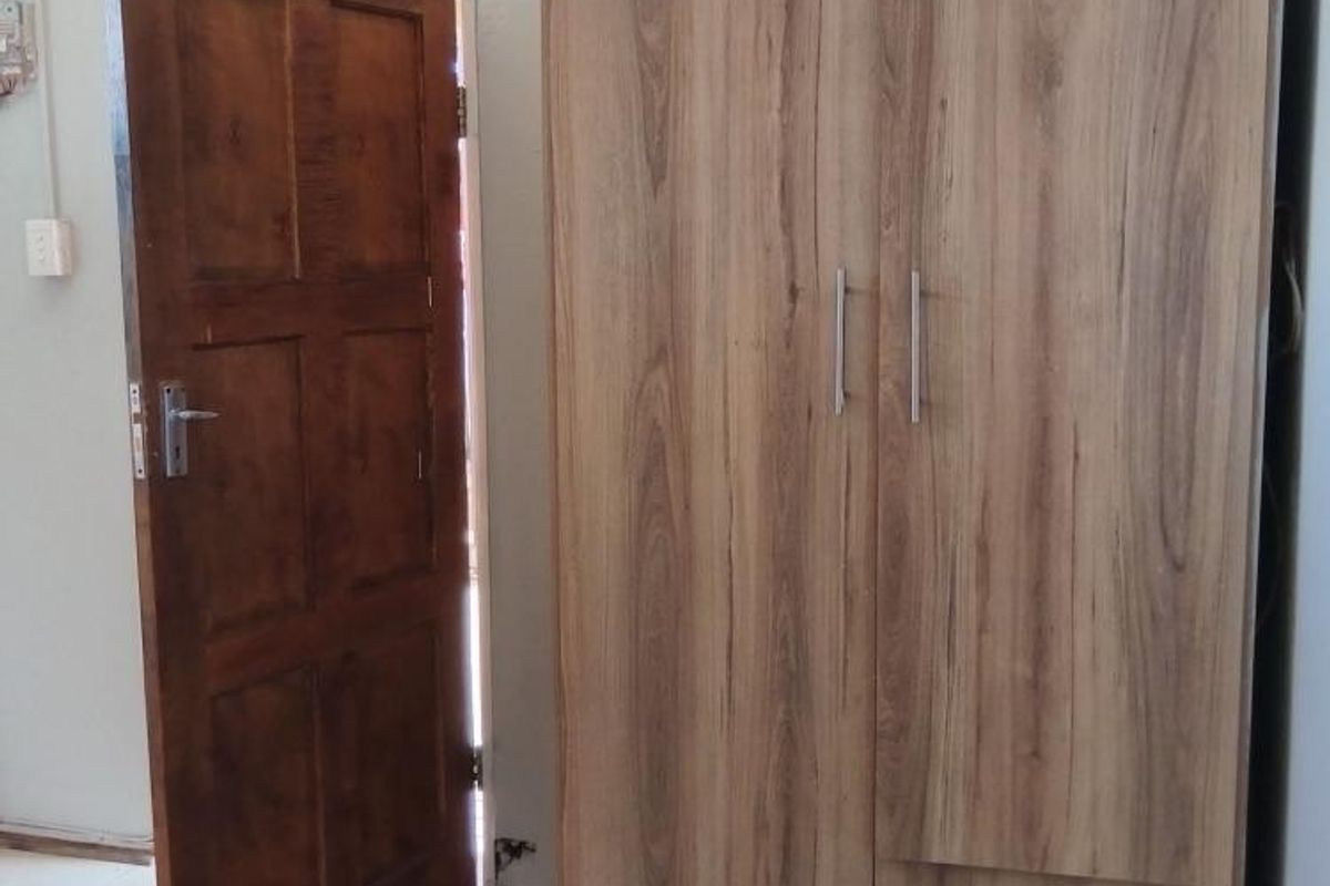 A bedroom interior featuring tiled flooring, a timber door, and visible electrical wiring along the wall.