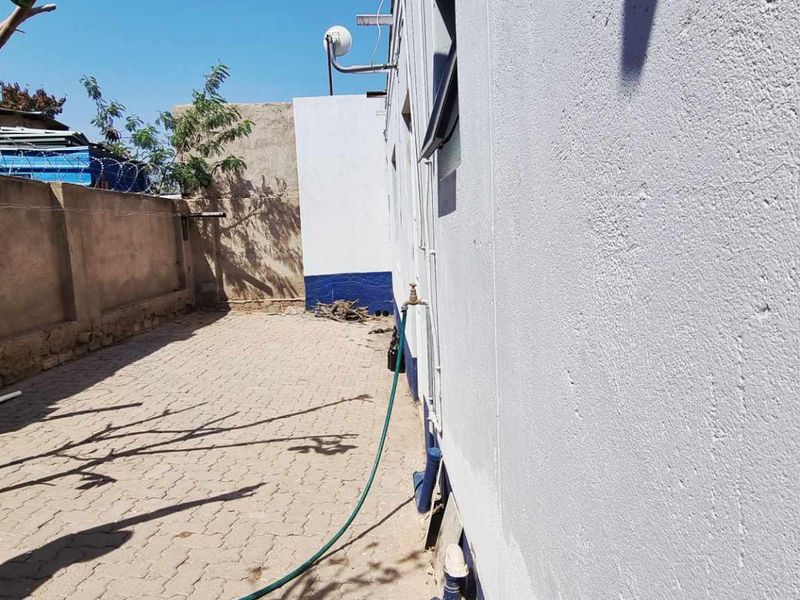 A side courtyard area featuring paved flooring, a perimeter wall, and an external water tap.